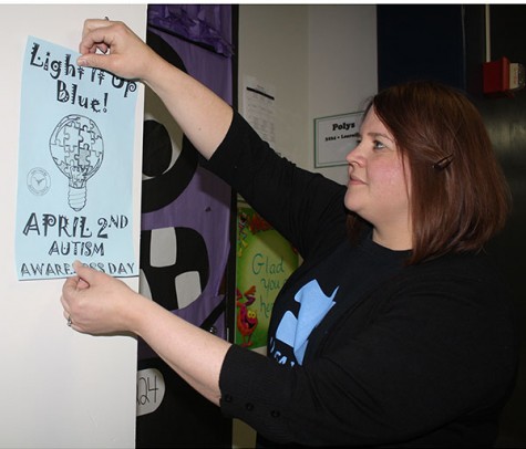 Theatre educator and director Amie Gossett, a passionate advocate for Autism Awareness, places Light it Up Blue posters around the school.