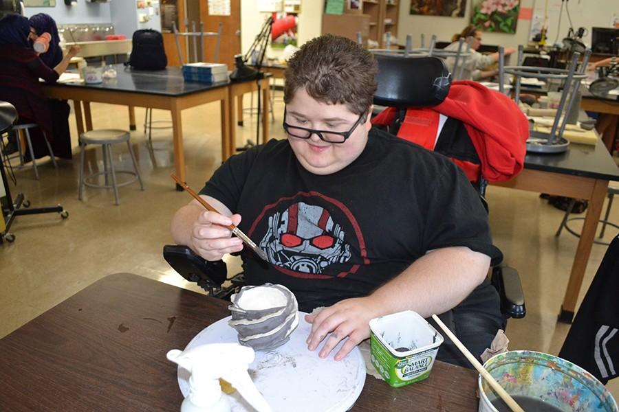 During Ceramics class junior Alex Rossi glazes his pot before it is fired.