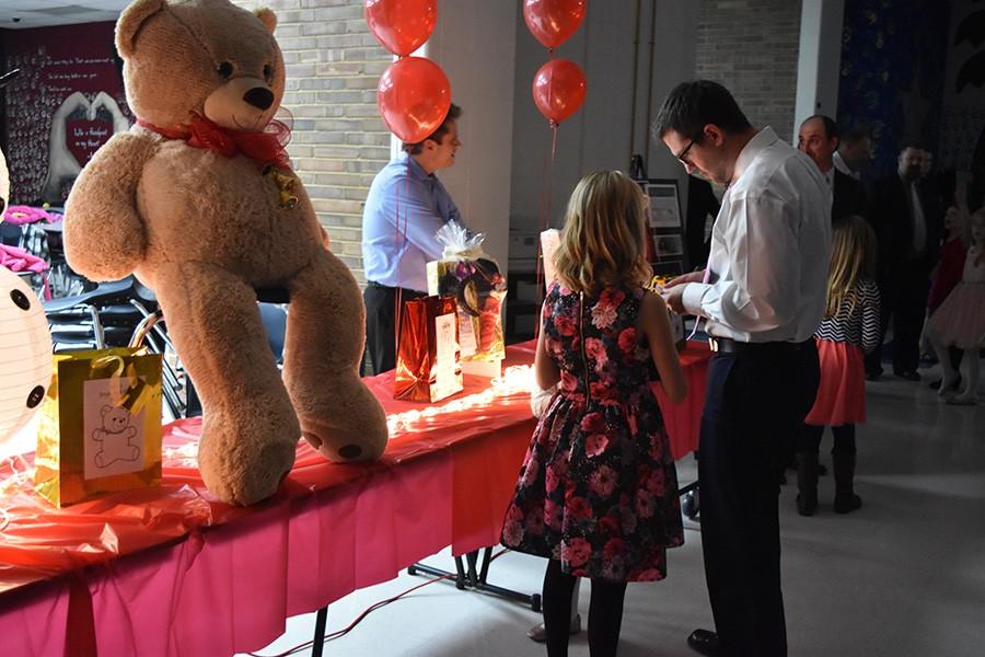 Guidance Counselor Chris Lorenz and his older daughter, Sienna, look at the giant bear as they put their tickets in for the raffle.  Different princess and lacrosse themed packages were raffled off in addition to the American Girl doll to encourage girls to attend the event.  “The girls getting dressed up was just magical and having the opportunity to take both of them, well, I didn’t really have any choice,” Lorenz said.