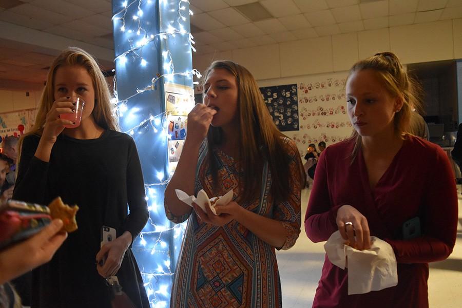 Seniors Jamie Gardner and Lauren Sanford eat laid out snacks at the Jingle Bell Ball with junior Hope Sanford.  The girls lacrosse players volunteered at the dance for elementary schoolers, which was put on by the team to raise money for the upcoming season.  “We sat there and ate goldfish and the assortment of cookies and drank pink lemonade after helping escort fathers and daughters to the cafeteria,” Gardner said.