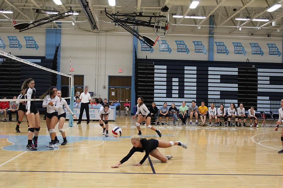 Others on the bleachers watch as senior Grace Goedde leaps and slides to reach the ball. Caroline Shaw ran to the center of the court to get the ball over. 