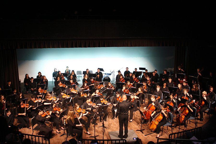 Directing the orchestra at in the theater, Mr. Sandheinrich waves his arms to conduct his students.