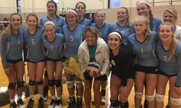 The varsity girls volleyball team huddles around Coach Dean in celebration of her 1,000th game. 