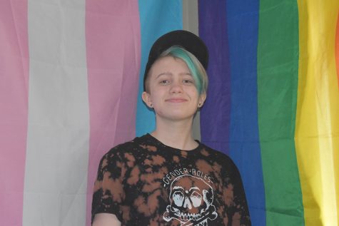 Posing in front of the transgender and gay flag, freshman Leslie Seay wears their they/them hat.