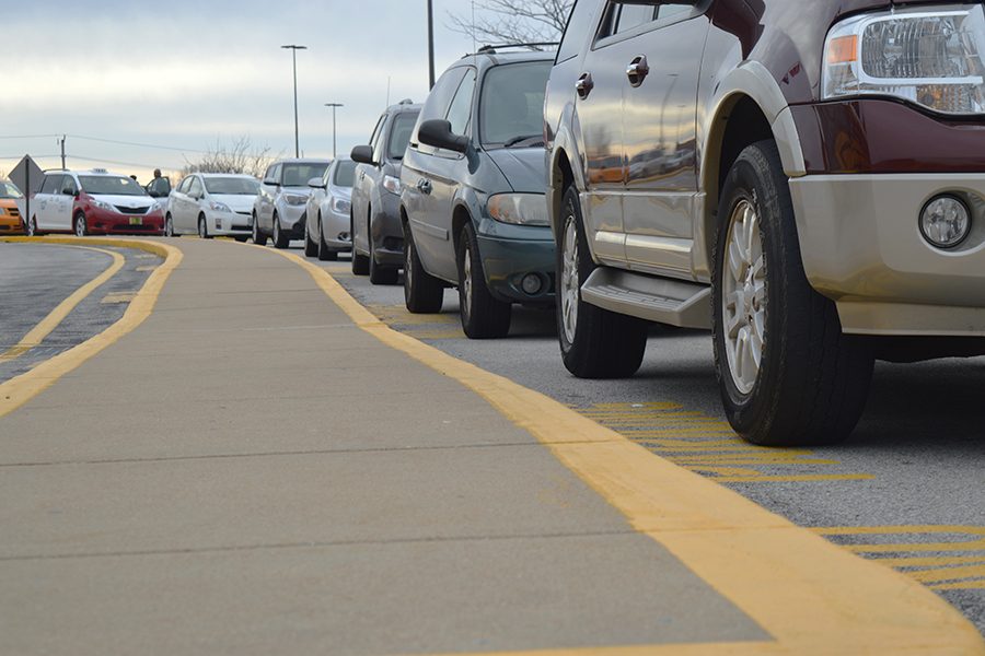 A long line of cars wait in the parking lot to exit the school. 