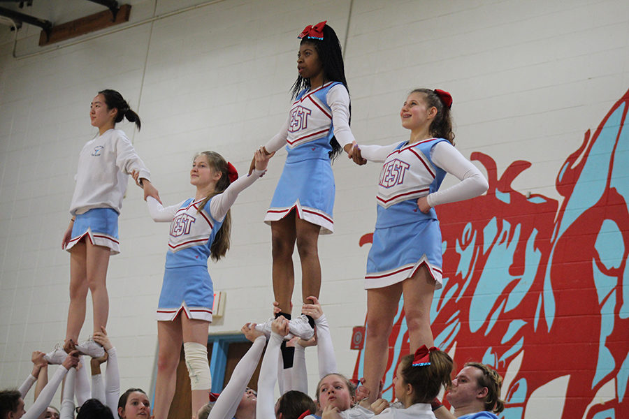 JV flyers Nayeon Ryu, Ava Pfeil, Jameah Collins and Emma Wallace grab hands in the air in a stunt formation at a JV basket ball game. 