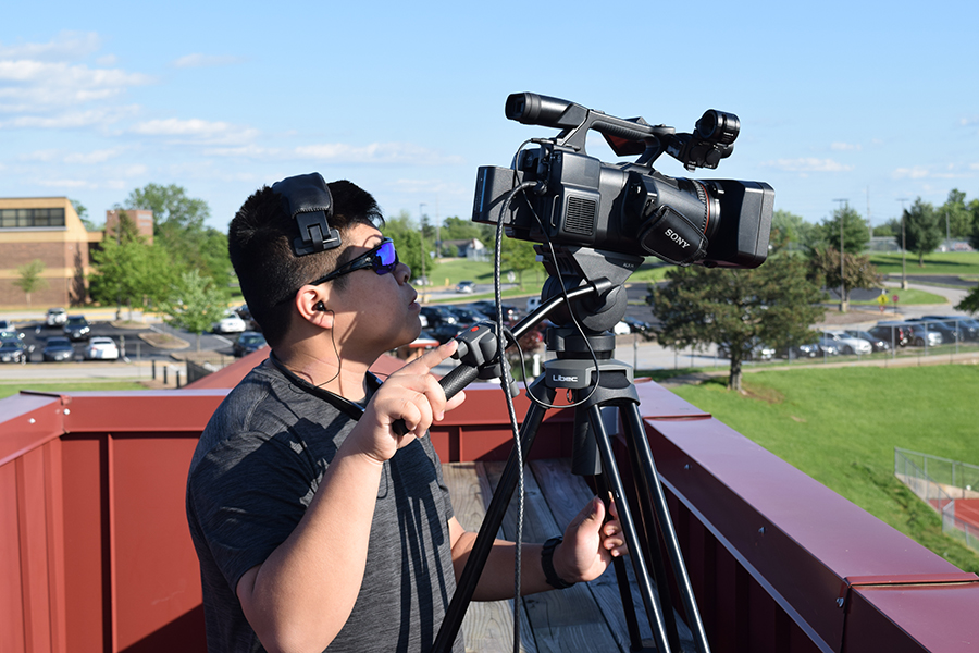 On top of the press box, sophomore Cameron Sato captures one of the camera angles of the game below. Sato worked behind the scenes to broadcast football, lacrosse and soccer games. “It was kind of like a live football game, all our footage switched between multiple cameras on the field or on top of the press box, and was then sent to the board,” Sato said. 