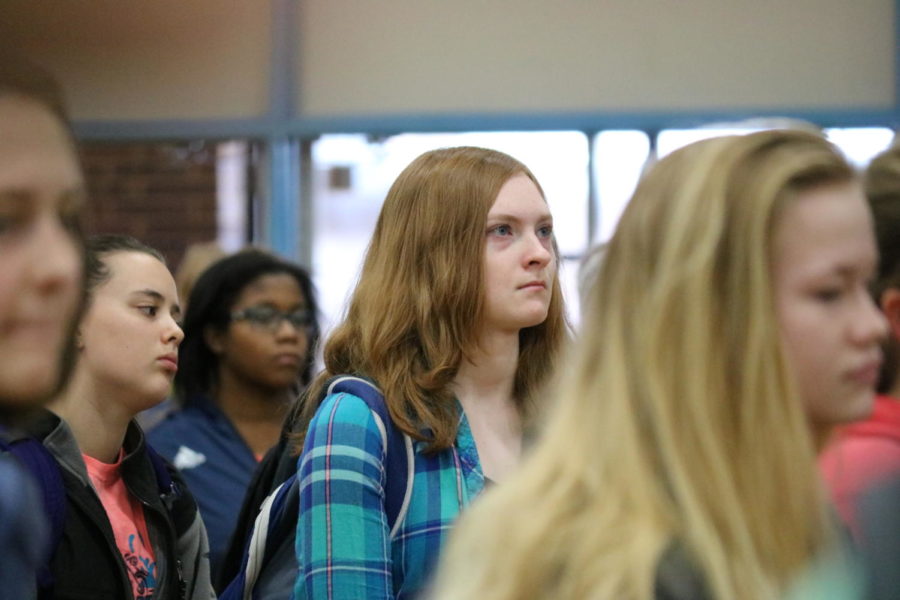 Sophomore Maddie Hoffman solemnly listens to speakers as they speak about recent school shootings in United States. Over 200 students joined Hoffman in the gym. “I really wanted to do something to support the cause, even if that just showing my support at the walkout,” Hoffman said. “Some of the information really hit me hard and strengthened my resolve to help.”
