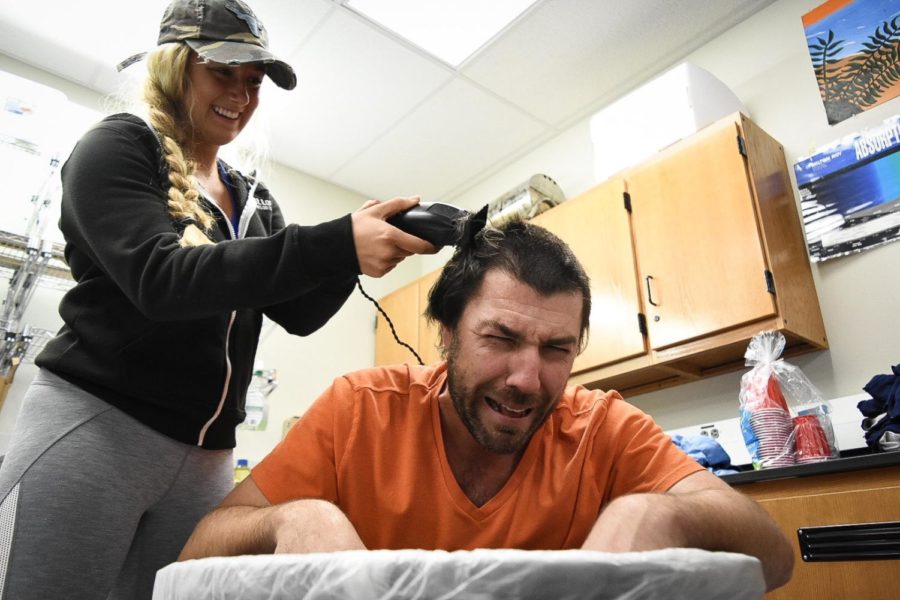 Gripping the electric razor, senior Sophie Pellegrino shaves coach Charles Cutelli’s head in his classroom after school on Thursday. Cutelli promised the girls cross country team that they could shave his head if they placed second in state. “Ive always known him as the guy who writes my workouts and tells me what to do, but then I shaved his hair off his head,” Pellegrino said. 