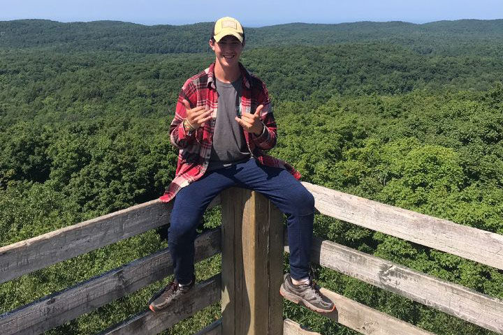 Sitting atop the viewing tower fence, junior Nathan Clem celebrates making it to the summit of the Porcupine Mountains. Clem and his friend Jacob Carpenter led a week-long expedition in the mountain range that included a trip to the summit.
