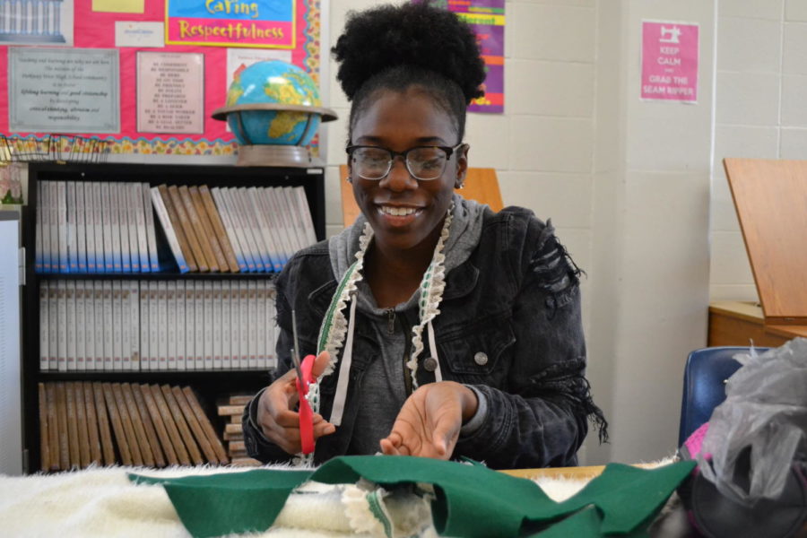 Cutting fabric with scissors in hand, junior Meela Abbey decorates her ugly Christmas sweater during a Fashion Club meeting after school on Nov. 29. Members of the club gathered in Family and Consumer Science teacher Renee Broemmelsick’s room to make their own holiday sweaters. “Since they were supposed to be ugly, I had to make mine ugly, but like a cute ugly, it had to have some potential,” Abbey said.