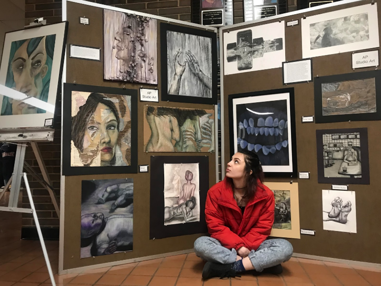 Sitting criss-crossed in front of her concentration, senior Allani Gordon showcases her work at the Parkway West District Art Show on Thursday, Jan. 24. Throughout the semester, AP art students focus on one theme, or concentration, to guide their projects. “I chose decay and wanted to depict beauty within decomposition with a feminine touch,” Gordon said. 