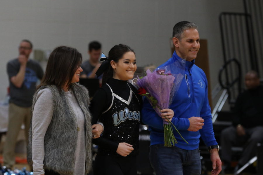Walking across the Main Gym on Wednesday, senior Sophia Ferretti is accompanied by her parents, Pete and Tonya Ferretti during the senior Poms ceremony. As the dancers walked, history teacher Zaven  Nalbandian announced the dancers achievements throughout their high school career. “It was a very bittersweet night,” Ferretti said. “I was really happy to have made it this far and I am proud of everything that I have accomplished. I definitely had to fight back my tears when the reality of not being on the team anymore started sinking in.”
