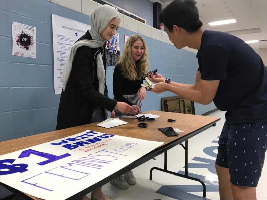 Selling an “I STAND WITH REFUGEES” wrist band to junior Jon Ma during second lunch, junior Sabrina Bohn and sophomore Ulaa Kuziez raise awareness for the Immigrant and Refugee Women’s Program. The feminist club voted earlier in the year to provide money to that group in order to expand their impact on the global community. “Last semester we had a group vote between three different charities. We had one that was a womens shelter that helped women who experienced domestic abuse, the Immigrant and Refugee Women’s program and another womens shelter with a different focus. The group members voted and decided on the Immigrant and Refugee program to bring awareness, not just in our community and school, but to a bigger world,” Bohn said. Photo by Kathryn McAuliffe