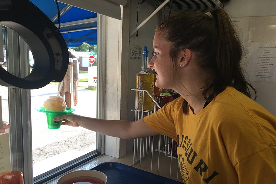 Handing a snow cone to a customer, employee and junior Audrey DeYoung fulfills her childhood dream of working at Tropical Sno Manchester, where she makes minimum wage. To reach a teenage demographic, DeYoung and her coworker created the Instagram account @trosnomanchester in hopes of having more teenagers drop by as customers. “What drew me to it was that it’s such a little shack and kind of a unique job to have,” DeYoung said. “Everyone I know goes there pretty often, so I knew I’d be able to see a lot of people from school. It annoys me when my friends are getting snow cones together, and I can’t be with them because I’m working.”
