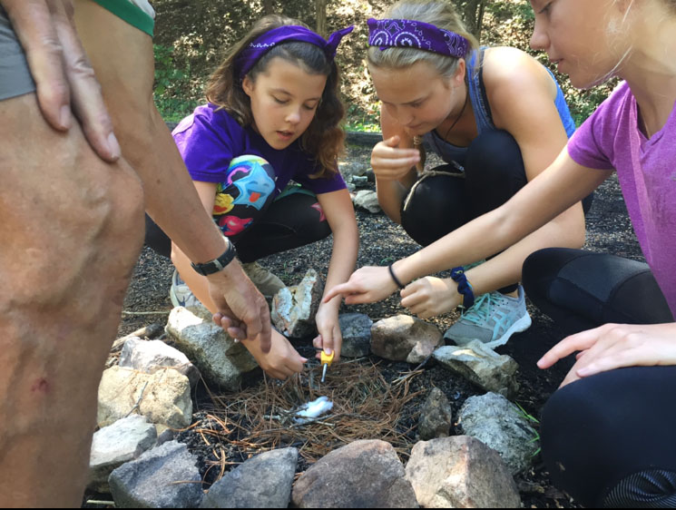 Bending down to help build a fire, sophomore and sixth grade camp counselor Anna Newberry coaches her camper, Rachel Ferguson, in using a flint and steel Aug. 28 at Camp Lakewood. Newberry attended Camp Lakewood as a summer camper, sixth grader and now counselor. “This is my first year as a cabin leader, but Id gone to summer camp five years before that. It was really fun to watch the girls start out as not super close friends because it was the beginning of the school year. They didn’t know each other, but they bonded a lot,” Newberry said.