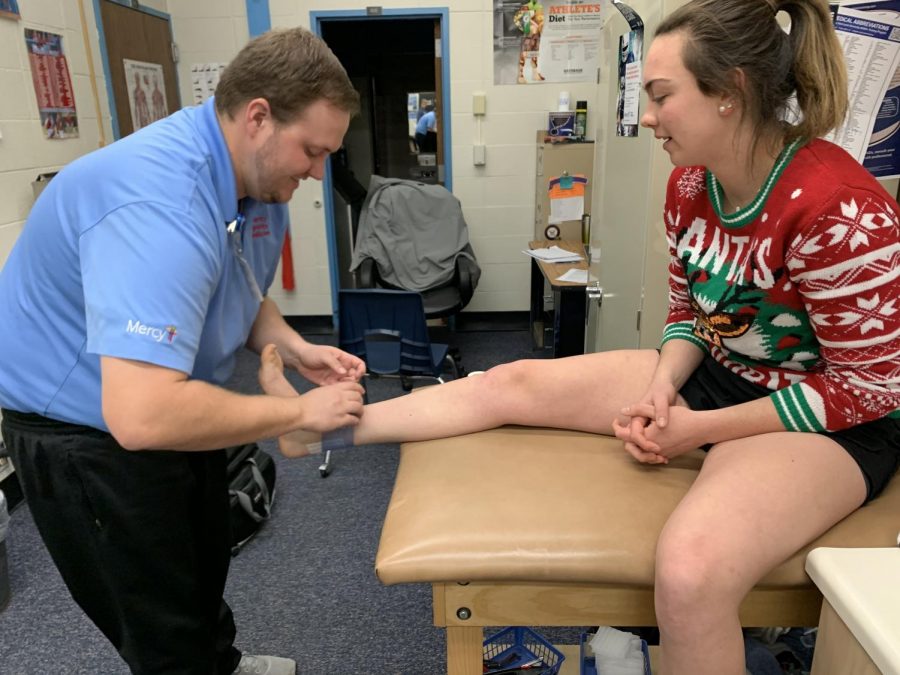 Putting+on+an+ankle+wrap+after+a+previous+injury%2C+new+athletic+trainer+Daniel+Smith+helps+sophomore+Sydney+Slaven+prepare+for+practice.+Through+Mercy+Sports+Medicine%2C+Smith+attends+all+athletic+events+to+make+sure+athletes+are+being+treated+for+injuries+on+and+off+the+court.+%E2%80%9CBeing+a+trainer+can+be+very+exciting%2C%E2%80%9D+Smith+said.+%E2%80%9CYou+never+know+whats+gonna+happen%2C+and+you+have+to+be+prepared+for+everything.%E2%80%9D