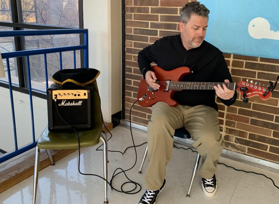 History teacher Mel Trotier plays his guitar during the passing period to collect donations for the anual Social Studies Department  canned food drive. Trotier began this tradition four years ago, to bring awareness to the fundraiser and raise money. “Even in a wealthy community, there’s still so many families that don’t have money to even eat through the holidays,” Trotier said. “I think it’s an important issue to bring up to kids that may not realize that somebody sitting in the classroom with them needs food.”
