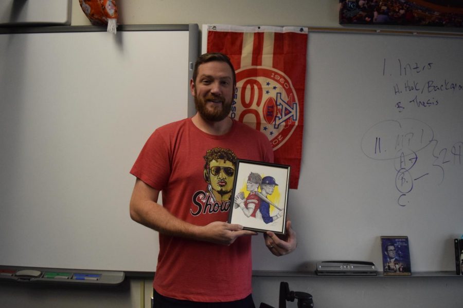 Holding a Kansas City sports themed picture, English teacher Casey Holland displays his classroom adorned with Chiefs decor. Holland will watch his favorite NFL team compete in the Super Bowl for the first time in his life Feb. 2. “I was born and raised a Chiefs fan. Im from Southwest Missouri two hours south of Kansas City. My friends and I in elementary school all liked the Chiefs and our parents liked the Chiefs and we used to go to games all the time. I was just born into it.