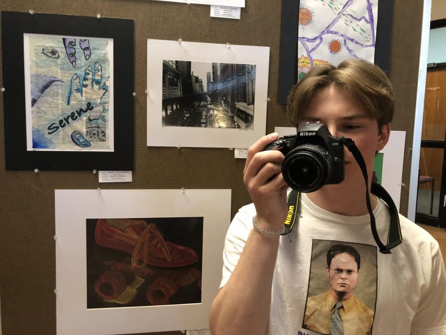 Camera in hand, senior Will Sloan prepares to take a picture of other art in the gallery. To his left is a photo that he shot in Chicago. “This is a picture of Lakeshore Drive. Its a famous road out of Batman, [and] that was one of my favorite movies as a kid,” Sloan said. “There’s a scene where the Batmobile goes through there, so I was like ‘I’m going to need a picture of that road.’’’