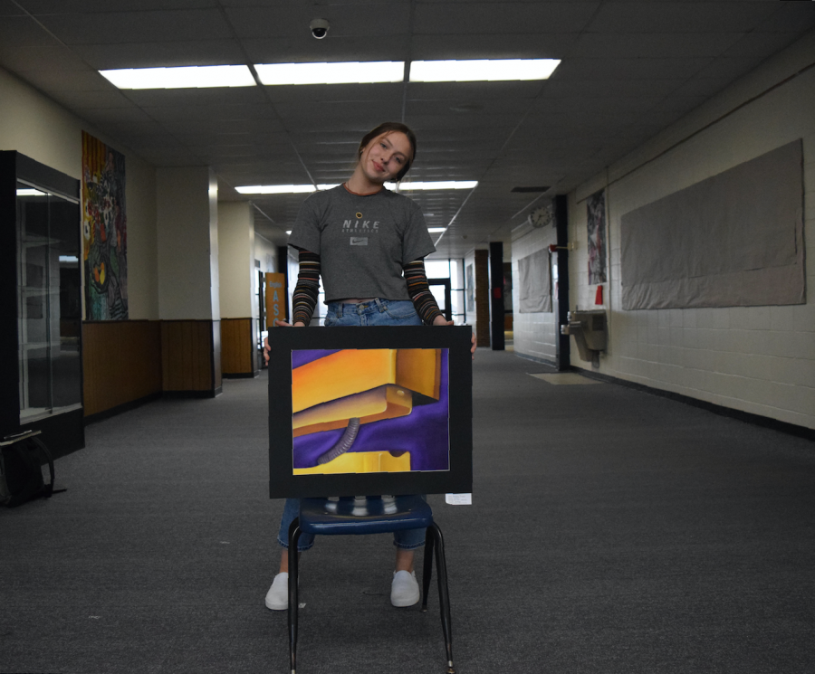 Junior Maddy Truka shows off her painting of a stapler. Truka has taken seven art classes in three years. “I love art because I use it to express myself and let out my emotions in a different medium other than talking,” Truka said. “I was proud of myself and happy that it was displayed next to other talented people; it’s nice to have validation for something that you love.”