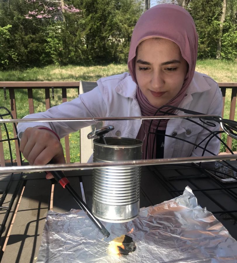 Lighting a potato chip on fire, junior Ulaa Kuziez completes a lab at home for Chemistry eLearning. Through combustion, students were able to measure temperature changes of different foods to determine their energy. “Completing the experiment at home was different than at school, but it was fun to create my own set up for the experiment,” Kuziez said.