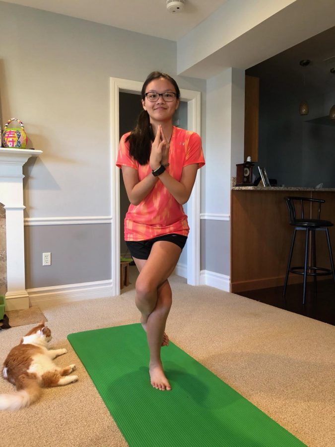 CAPTION: Junior Tiffany Ung, along with her cat, poses for her Yoga class, which takes place over Zoom.