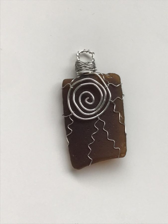 Will Be For Sale: Brown Sea Glass Pendant - One piece that was frustrating was the sun on brown sea glass, Gleason said. Although I really like the way it turned out, the wire kept springing back up and not staying in place. To deal with that, I put on good music and try to stay positive. Sometimes I have to restart, but usually, I can figure it out. Once I finished it, it ended up being one of my favorite pieces.