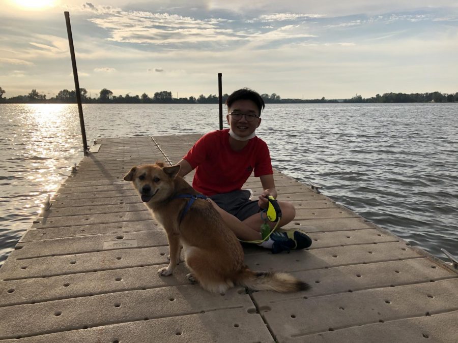 Pulling down his mask for a photo, senior Justin Xu smiles with his dog. 