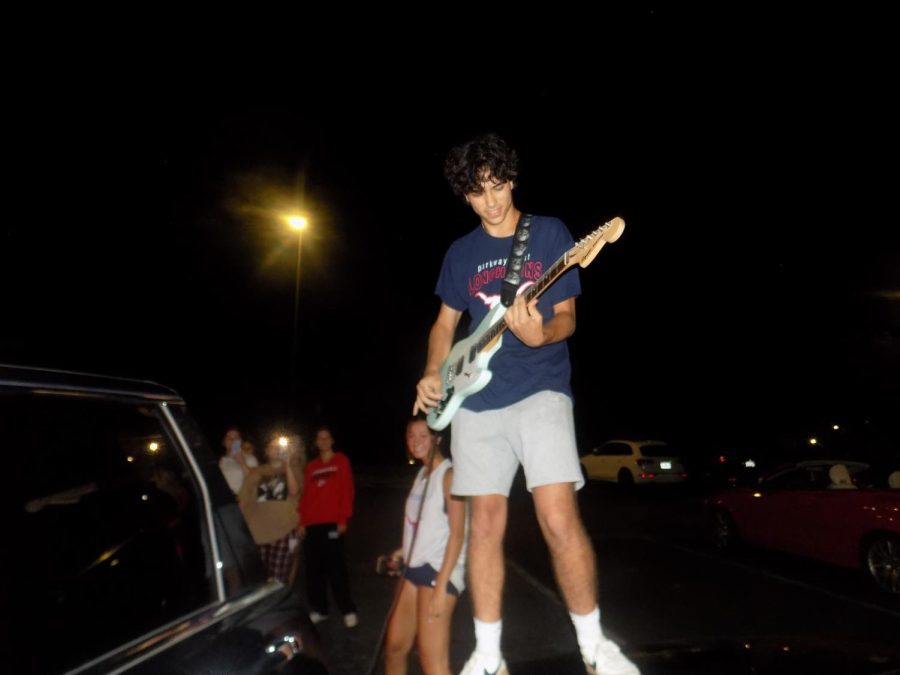 Playing along to Kiwi by Harry Styles, senior Santi Calvo stands on the hood of a car and performs for his classmates. Calvo began learning how to play the guitar six months prior. It was my first time playing guitar in front of more than one person, so even though it was in a parking lot it felt like a stadium concert, Calvo said.