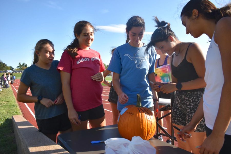 Sharpie in hand, junior Inaya Chishti signs this year’s pumpkin, a symbol of girls cross country. After this years pumpkin was revealed, everyone signed their name to promise a good season ahead. “The pumpkin was our mascot. Shes been with us since day one, [and] I think she keeps us going,” Chishti said. “The most exciting thing about the pumpkin was just the fact that it brought the team together. It was something that we bonded over and even if youre really fast, or if youre slower, everybody could be included in loving the pumpkin. Everybody took turns carrying the pumpkin and everybody bonded over the fact that our mascot was an inanimate object.”