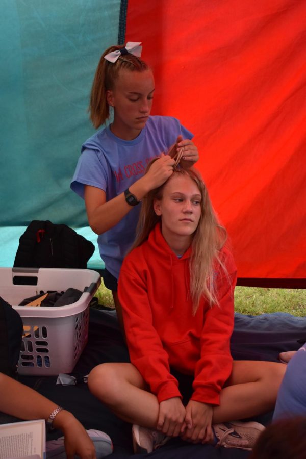 Preparing to race, junior Amy Rein braids sophomore Sally Peterss hair. As part of her pre-race traditions, Peters had her usual morning bagel with peanut butter and styled her hair into two dutch braids, tied up into a high ponytail. “I always liked to do a special hairstyle before I ran to make me run fast. Amy was a good braider and I’m not, so I had her help me braid my hair so that I had some pretty fly hair for the meet,” Peters said.