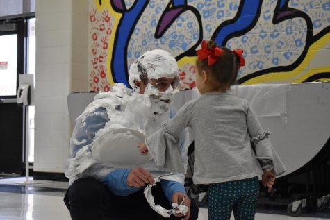 Greeting his 3-year-old daughter Molly McCabe, Principal John McCabe smiles after getting pied in the face by senior Esha Francis during lunch. McCabe got pied as a reward for school spirit at the Parkway Holiday Cup Volleyball Tournament on Wednesday Dec. 14. “[Molly] just started her first year of Pre-K and shes loving it. I told her all weekend I was getting pied and she thought it was really funny, so she just wanted to see dad getting pied. She loved it but she told me she was a little bit scared because she didn’t recognize me,” McCabe said.