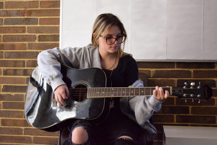 Playing+an+acoustic+guitar%2C+freshman+Noelle+McSpadden+sits+just+outside+of+her+music+classroom.+McSpadden+was+inspired+to+play+guitar+to+add+to+her+songwriting.+%E2%80%9C%5BGuitar+class%5D+makes+songwriting+much+easier+for+me.+I+feel+good+about+my+music+because+I+can+actually+play+with+a+guitar+%5Bto+back+it+up%5D%2C%E2%80%9D+McSpadden+said.