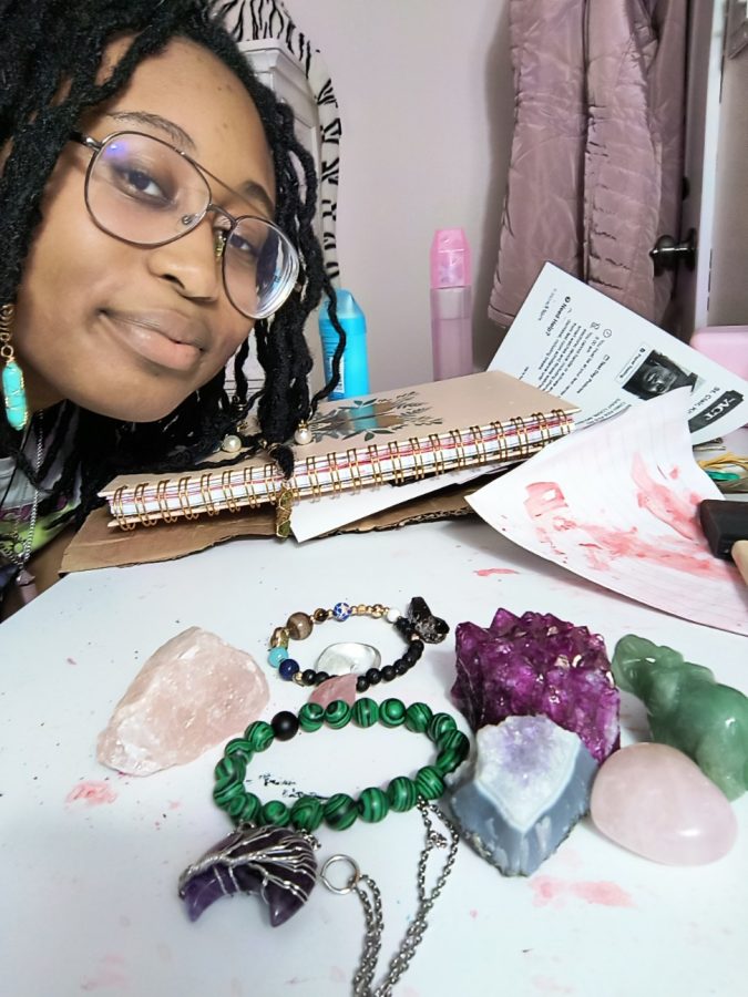 Posing next to rose quartz, an amethyst necklace, jade figures and other crystals, senior Bibi St. Clair shows off her crystal collection. 