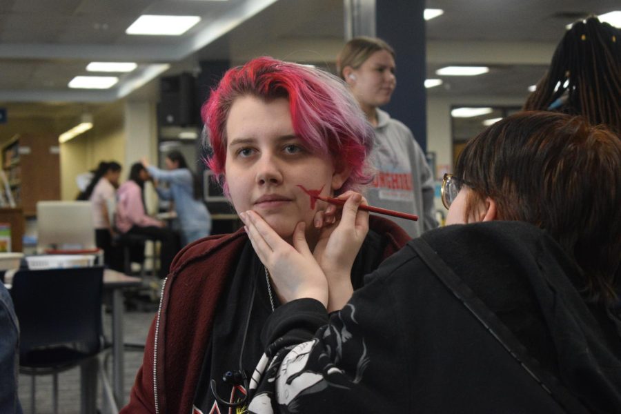 Tilting their head patiently, senior Macy Ziegler gets their face painted in the library in preparation for the Spring Pep Rally. The library invited students to come in during lunch and paint each other’s faces West-themed for the event. “[The event] sounded fun. [Face painting] is a thing I havent done since I was eight, and I had a friend who wanted to go, so I figured, why not? Its free,” Ziegler said. “I hung out in the library before school a lot last year with my friends, and I enjoyed it.”