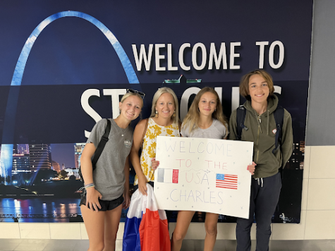 Sophomore Maddy Tarter and her family greet sophomore Charles Leleu at the airport in front of a welcome to St. Louis sign that features the Gateway Arch. Tarter and her sister hold a sign with French and American flags that reads: Welcome to the USA Charles.
