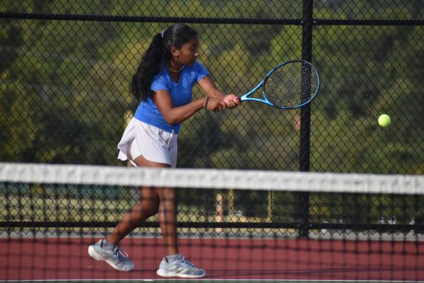 Freshman Mireya David stands in a tennis court, swinging her racket in front of her while stepping forward.