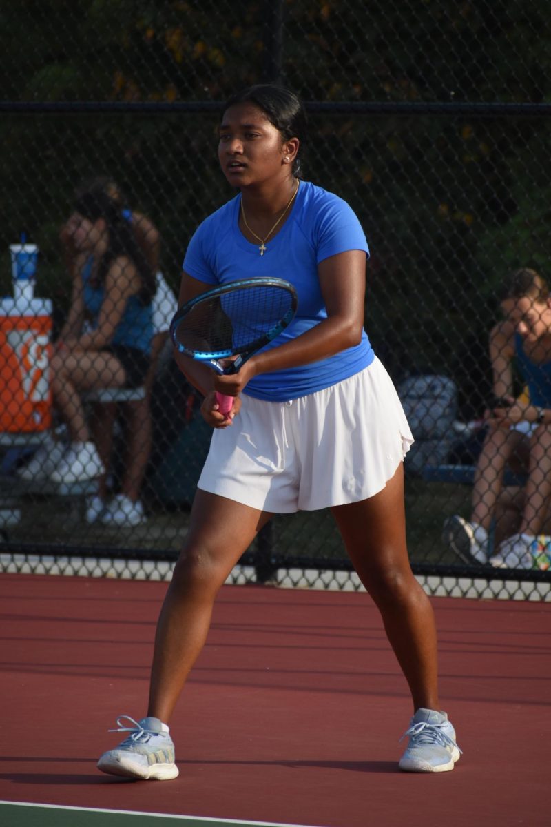 Freshman Mireya David holds her racket in front of her with two hands, gazing forward during her game. She stands in the center of a tennis court.
