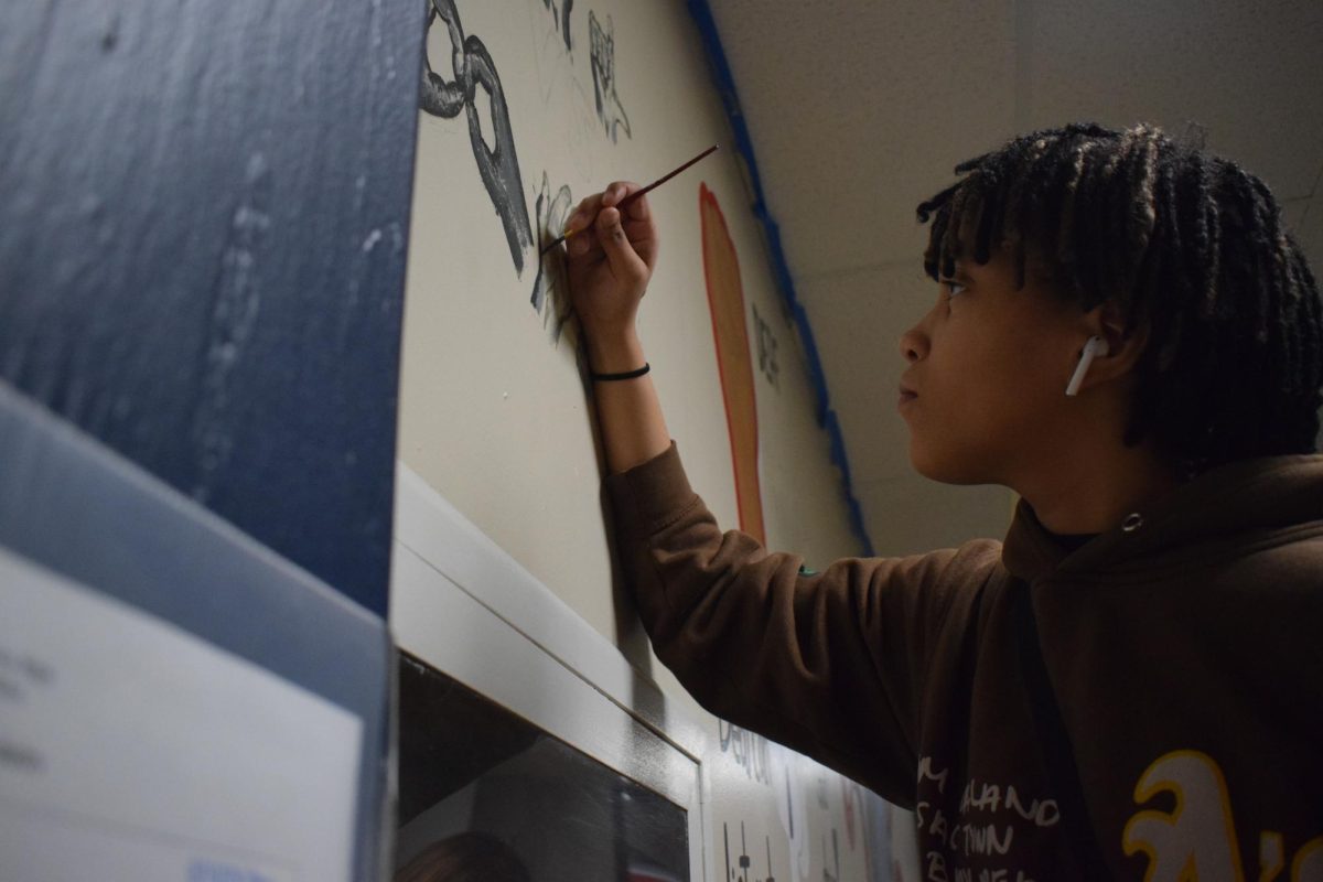 Focused intensely on her artwork, junior Jayana Shead works on a mural on the wall outside the classroom. American Sign Language 3 students studied techniques and meanings behind deaf artists work in their DeVIA art unit and collaborated on a mural outside the classroom. Often times, there are misconceptions about the capabilities of deaf people, so by creating this we are able to help people understand more clearly what deaf people are capable of, Shead said. This mural is important because it represents the struggles and common misconceptions of ASL, and working on something like this that will last on the wall for years makes me happy because its something that people will get to see every time they pass the hallway.