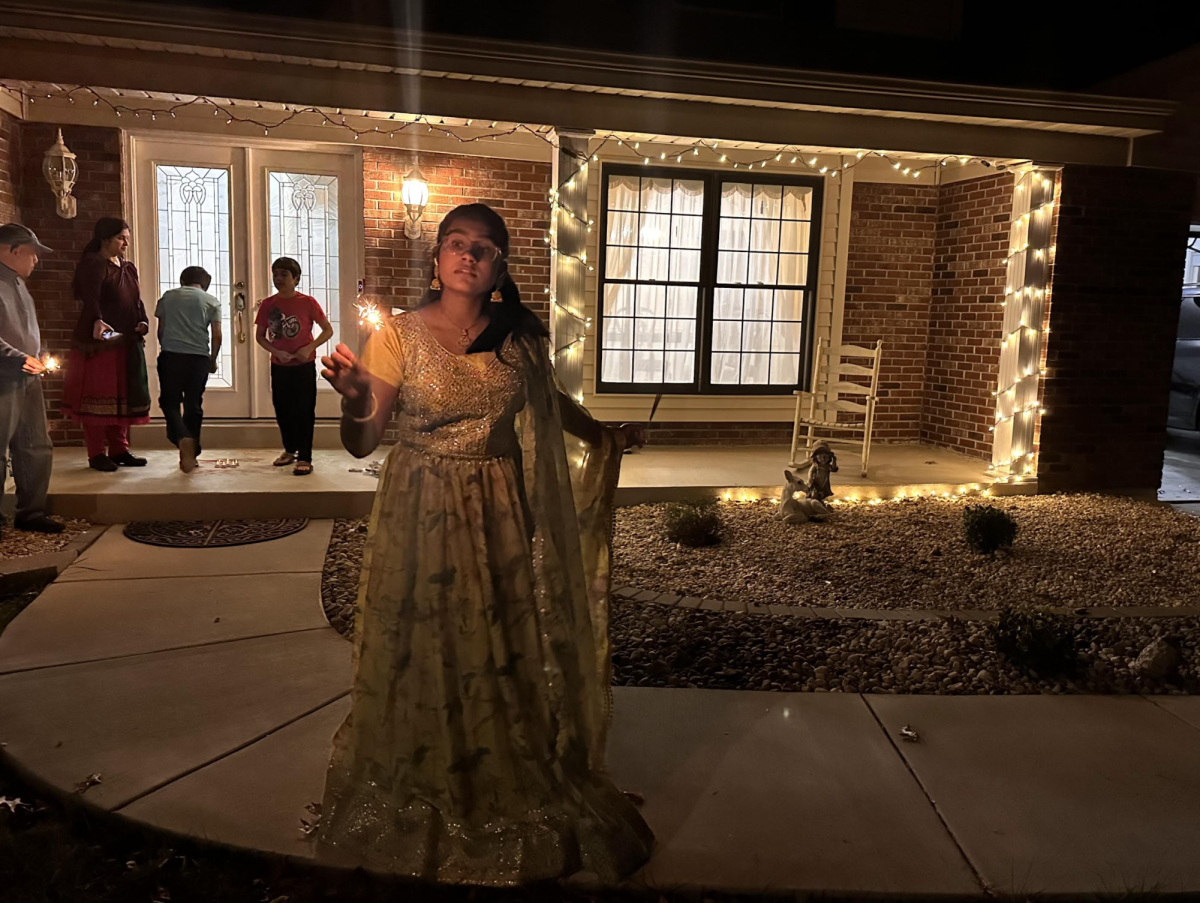 Sophomore Sravya Guda stands outside in a saree, lighting a firecracker at nighttime.