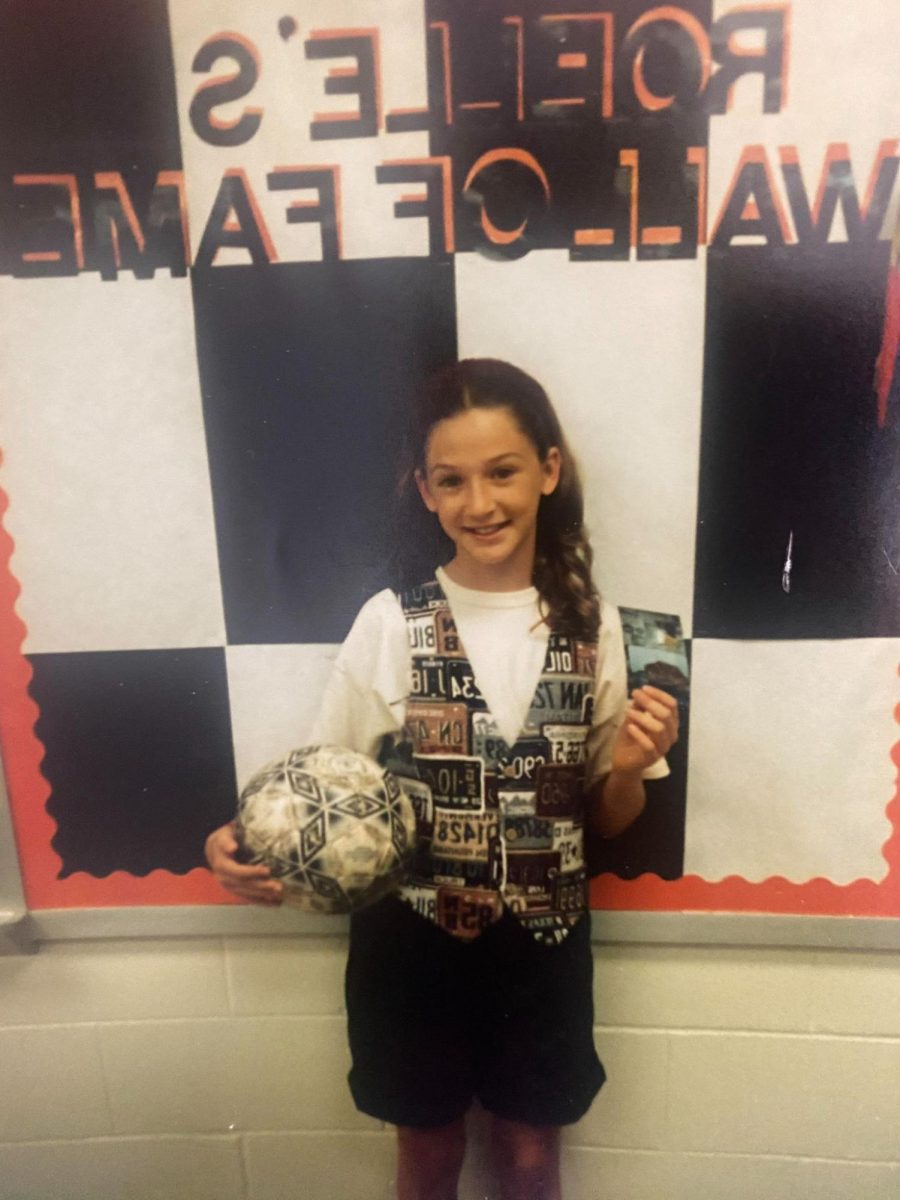 FACS teacher Katie Hashley poses with a soccer ball and a picture of her cat. Hashley brought the items  for a show-and-tell activity. “I brought my soccer ball, because at that time, soccer was everything to me,” Hashley said. “As for the picture, growing up, the only pet we had was this cat. She was my sister's cat and she was the meanest cat in the world. She always hissed at us and wasn't nice at all. We liked her, but I remember her being really mean to us. This picture just cracks me up because now I look at that vest and I'm like, ‘Man, that thing is so ugly,’ but when I saw it at the mall at that time, I was like ‘I have to have that.’ Everybody wore vests in 1993, so it was definitely a fashion statement [to wear one] with license plates on it.” 