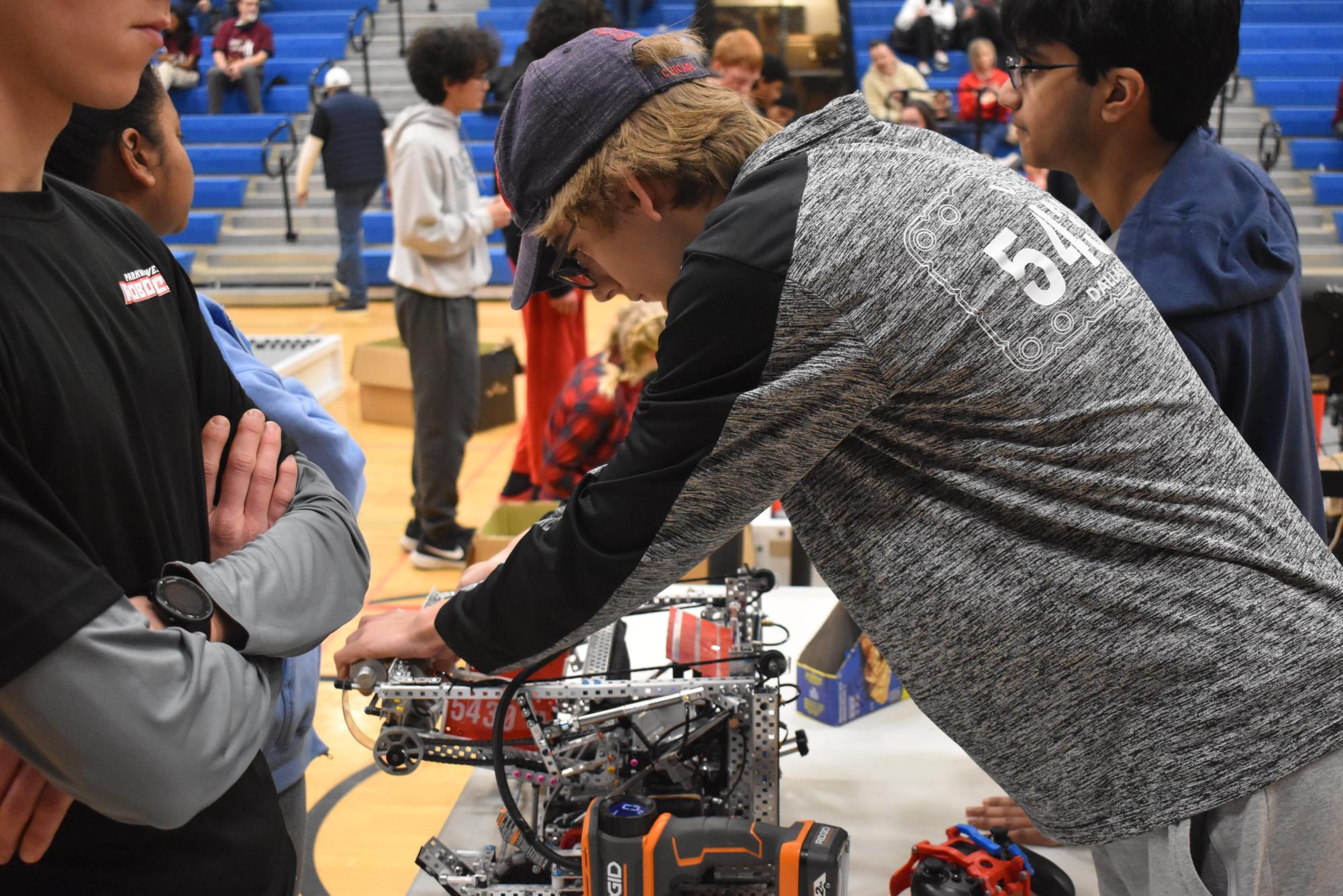 Peering through his glasses, Blue Brains Team Lead and senior Sawyer Ladd carefully examines his team’s robot in between contests. As team lead, Ladd seeks to encourage collaboration among his teammates. “We try [to] become more than just a group of people achieving successful robotics. On my team, Ive tried to make us more of a friend group than a robotics team. So thats improved our team chemistry — we just generally enjoy being around each other and that allows us to work together a little [better],” Ladd said.