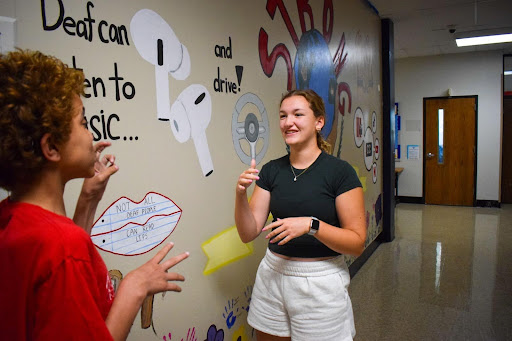 Standing in front of the American Sign Language program’s mural, junior Brooke Hoenecke signs with freshman Darren Young. Hoenecke began cadet teaching for ASL this year alongside working towards earning her seal of biliteracy. “I was in ASL class when I received the email [that I qualified for the seal]. I was jumping up and down with my teacher and the rest of the class. One of the reasons why I took cadet teaching this year was so that I could prepare for the Seal of Biliteracy and be immersed in ASL,” Hoenecke said. 