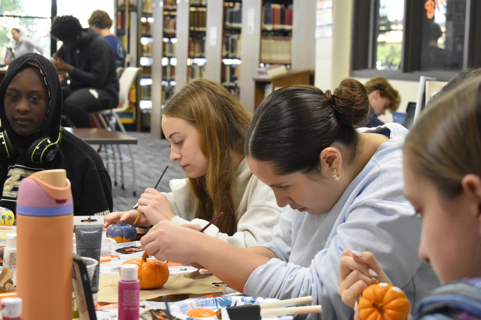 Concentrating on her pumpkin, senior Sophie Crutcher (left) paints with a small brush. As Best Buddies members painted Inside Out characters, Crutcher chose Sadness. “[My favorite part] is the experience of hanging out with everybody and seeing everyone’s pumpkins,” Crutcher said.