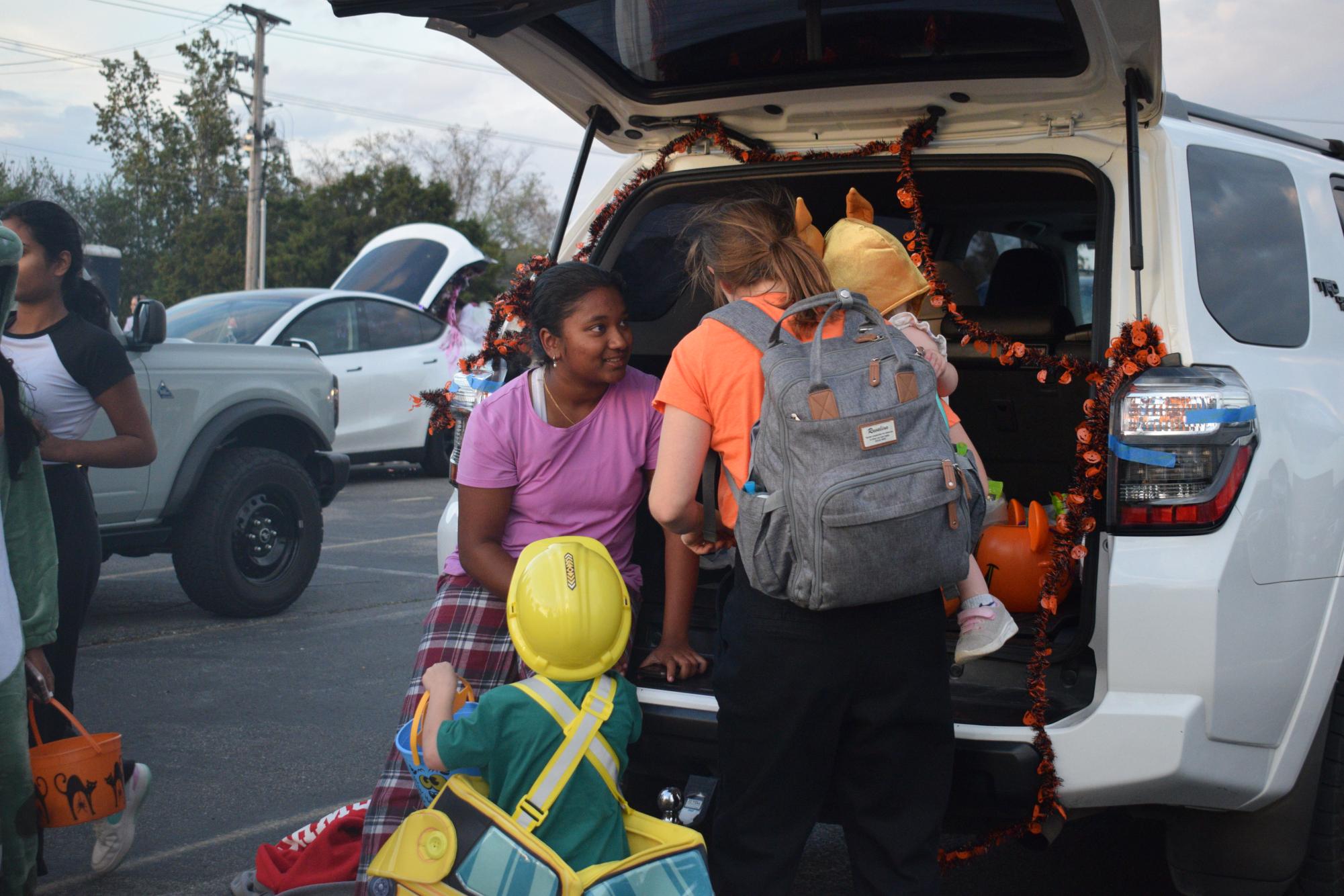 Leaning against a car, varsity girls tennis team member and sophomore Mireya David converses with a mother carrying a child. Members of the team joined together to celebrate Halloween and finish off the season with the trunk or treat event. “The little kids are so cute and seeing them dressed up in little costumes is a lot of fun,” David said.