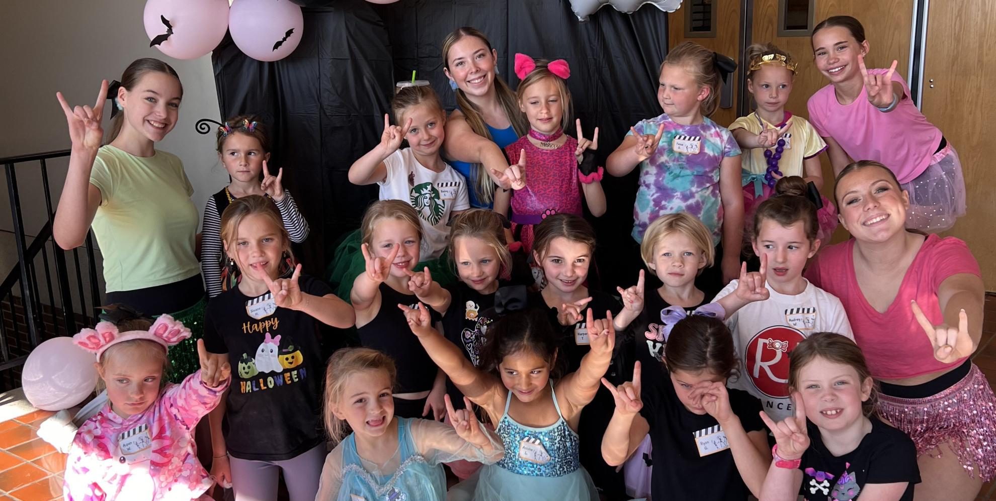 Posing with their horns up, junior Lily Overmann (back row center) directs the campers for a group picture with her teammates. Each camper and dance team member had the chance to dress up in their halloween costume of choice. “I think the best experience overall has just been the community of the dance team with everybody. I feel like most of the girls are all really close, and we have a lot of fun together, and that makes [the season] really fun. It’s not just like we’re all working by ourselves, it’s a group [effort],” Overmann said. 