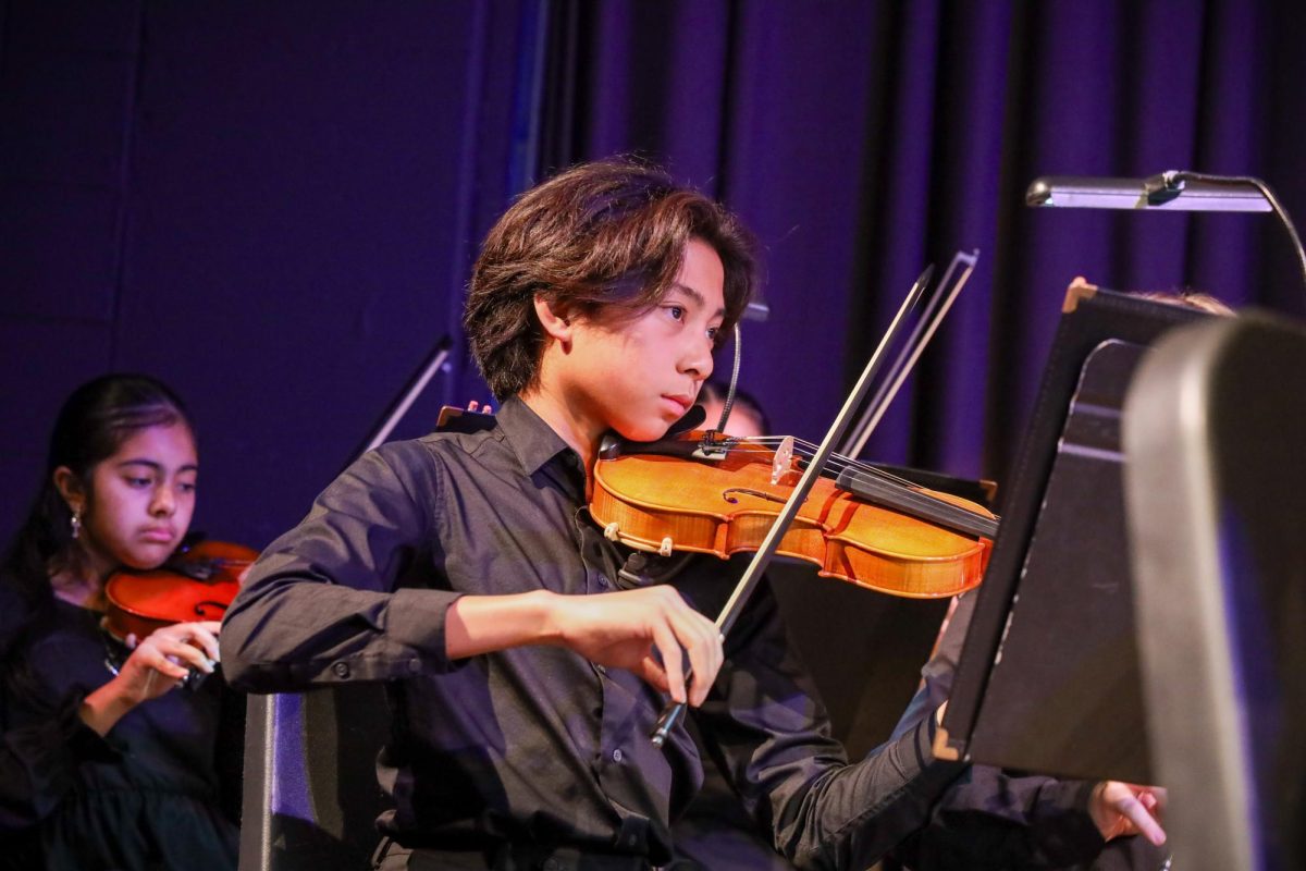 Gliding his bow across the strings of his violin, freshman Caleb Ople immerses himself in the music during the orchestra concert on Nov. 12. Ople has played violin since he was six and joined the orchestra in high school because of his parents. “[During the performance, I told myself] I hope I don't sound horrible when everybody's watching,” Ople said.