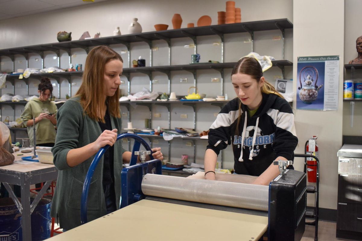 Eyes on the clay slab roller, social studies teacher Rachel Money learns how to use pottery equipment from sophomore Madeline Tipton during the “Teach a Teacher” AcLab event. Ceramics teacher Ashley Drissell hosted this event after receiving trinket dish pottery forms from a grant, which facilitated the process for teachers. “It was fun to take a break and be creative, [doing] something different with my day. It was really neat to get [teachers] into an art classroom with students [and] learning what they do in there,” Money said.