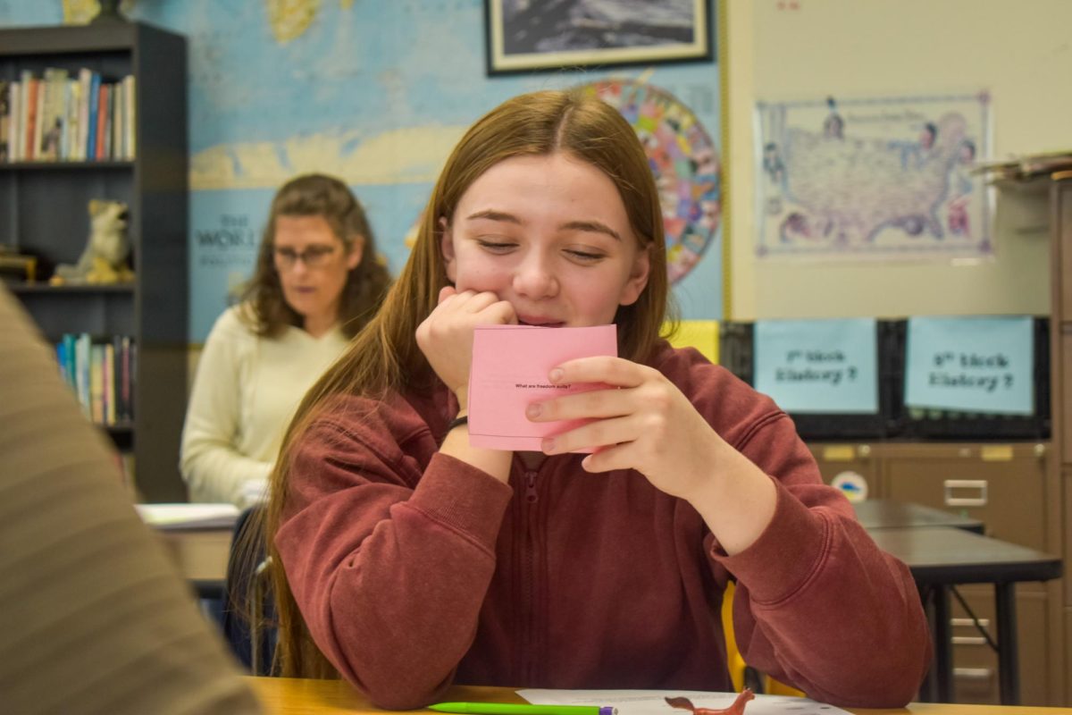 Reading the answer on the back of the card, freshman Madi Bell quizzes her classmates. Social studies teacher Lara Boles prepared a board game activity to help her US and World History 2 students study for their final. “I liked this activity because the answers on the cards were also the answers on the test, so it helped prepare for what you would see on the final. I [also] enjoyed having some competition against my classmates to see who knew the terms the best and who could make it around the board first,” Bell said. 